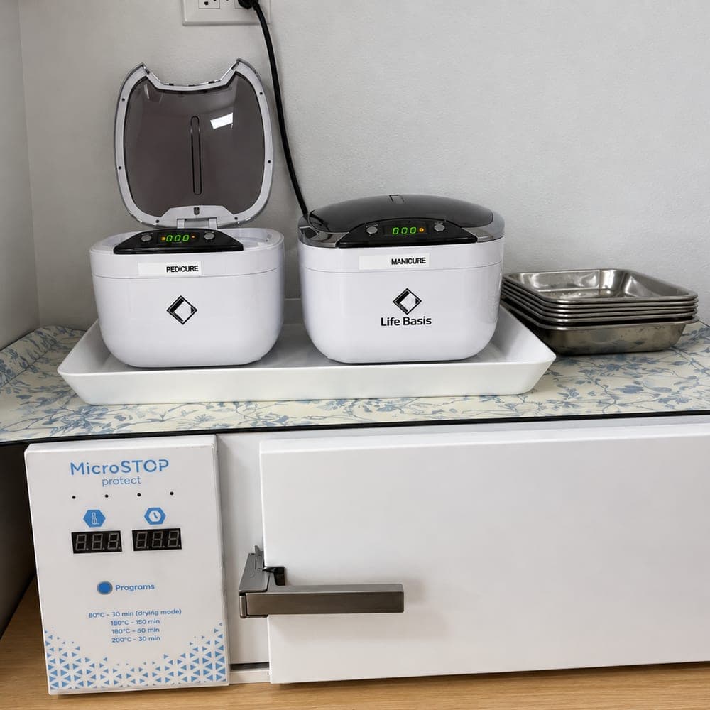 The studio’s sterilization station: a dry-heat sterilizer under two ultrasonic cleaners, one labelled pedicure and one manicure, with steel trays beside them