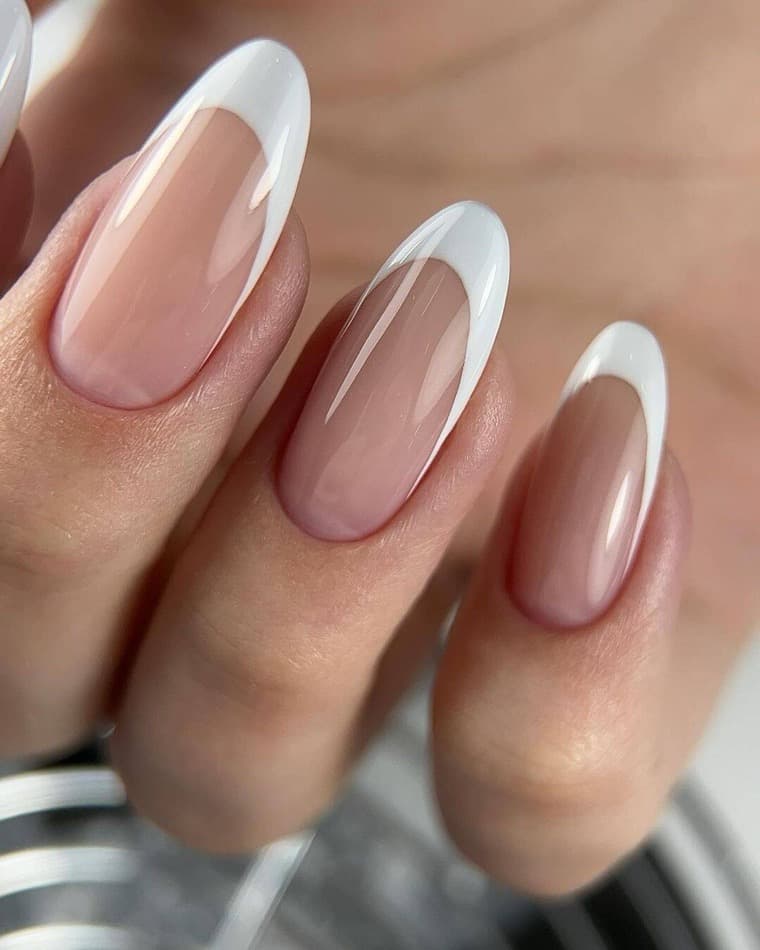 Almond fingernails with a white French tip over a sheer nude base