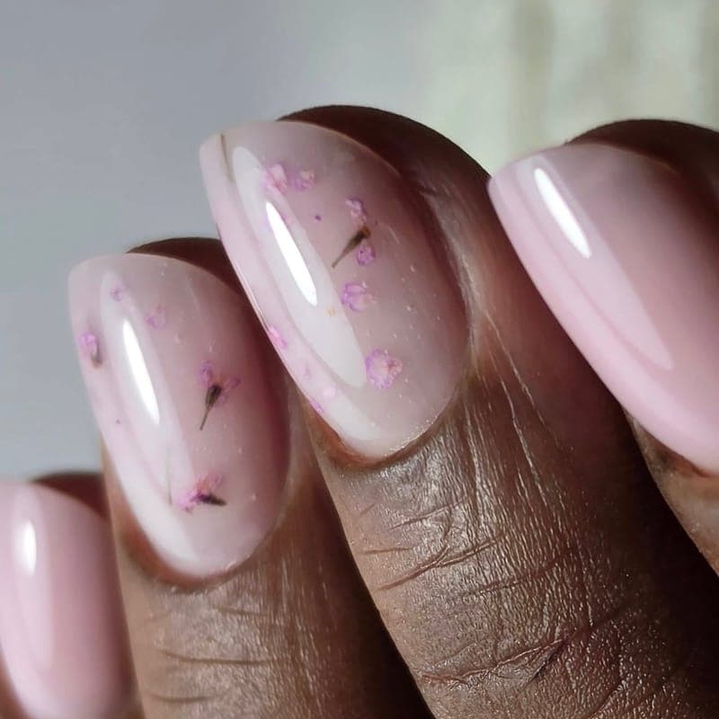 A close-up of nude pink nails with pressed dried flowers