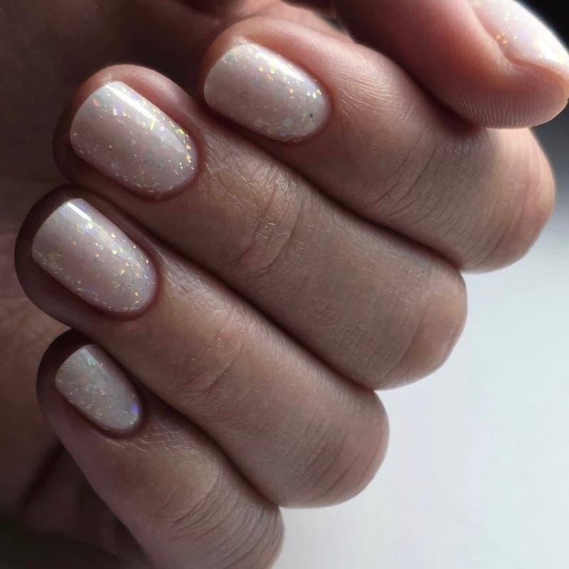Short nails in a pale cream with iridescent flakes