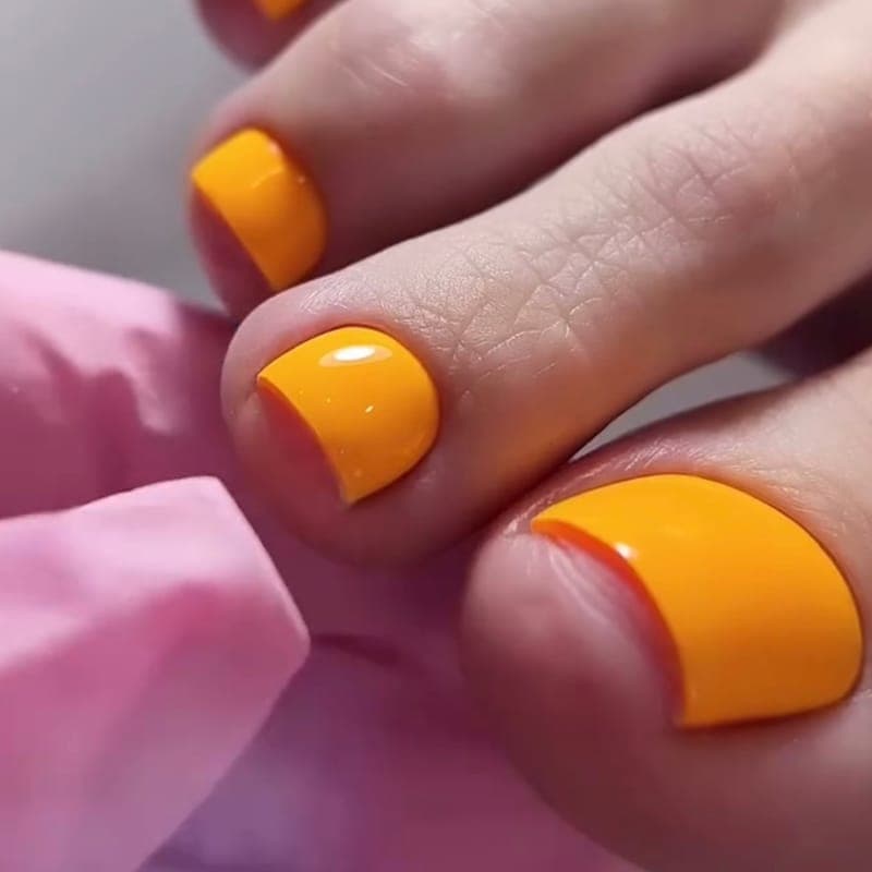 A pedicure in a bright orange gloss, a pink-gloved hand holding the toes