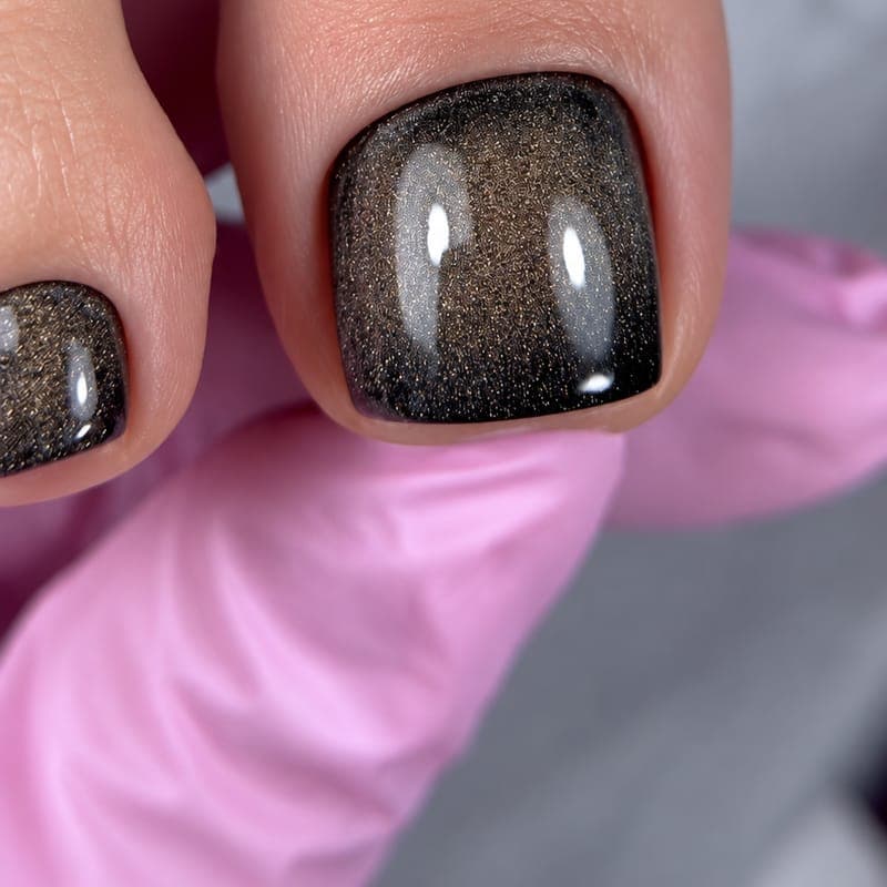 A big toe in a dark brown cat-eye gel with a soft shimmer, held on a pink glove