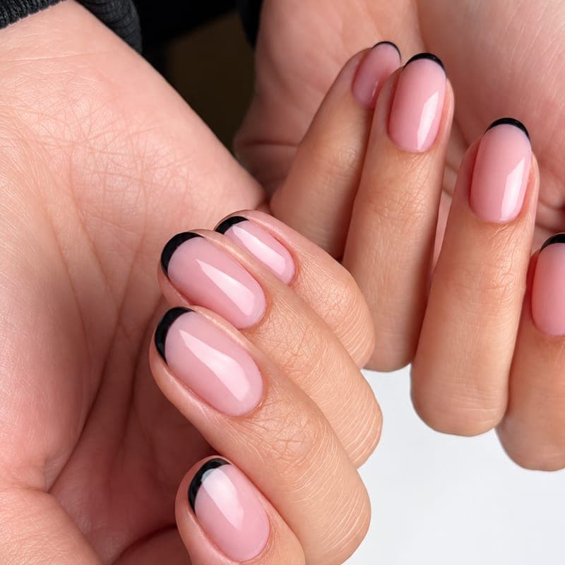 Short rounded nails in a sheer pink with thin black French tips