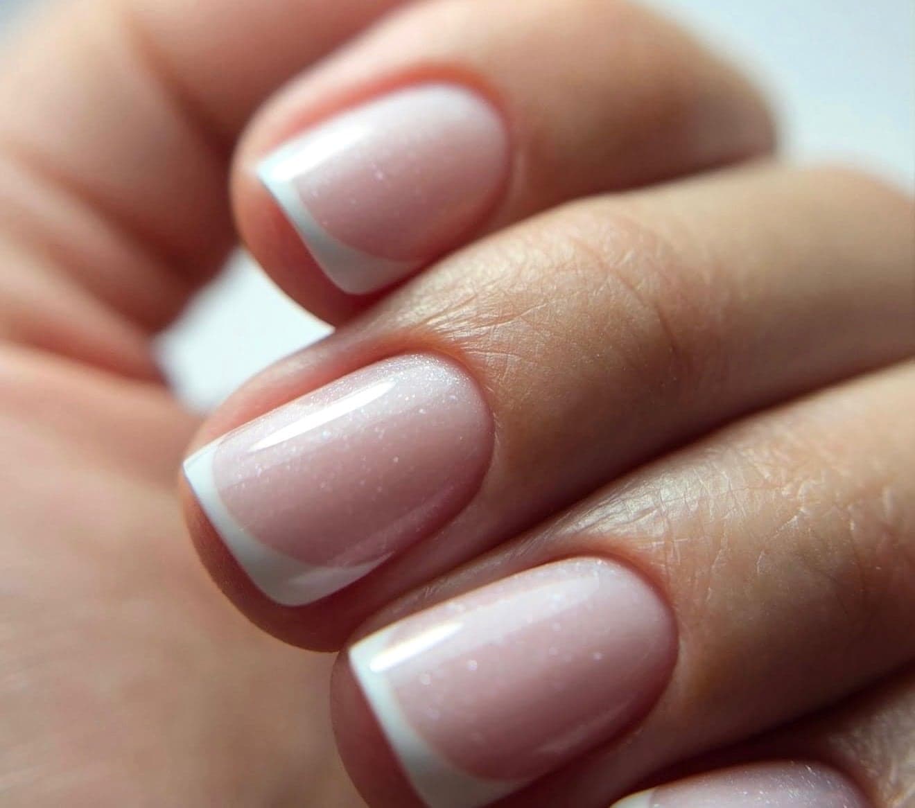 Short square nails with a white French tip and a soft shimmer, close up
